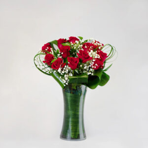 Red roses with baby breath and green in a clear tall vase